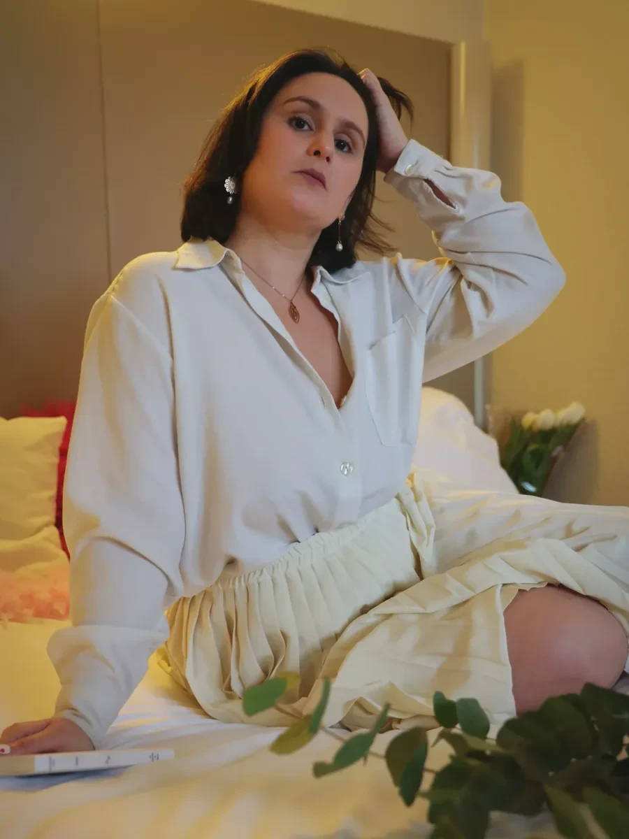 Gaarance en chemise crème, assise sur un lit